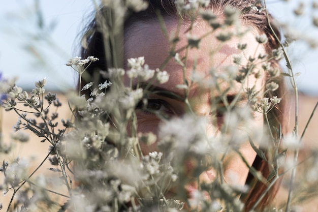 Jonge vrouw kijkt door een boeket van wilde bloemen op het veld.