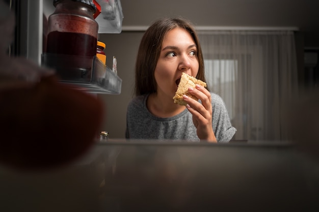 Jonge vrouw kijkt in de koelkast, uitzicht vanuit de koelkast, meisje eet 's nachts, angsten