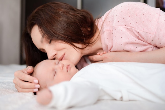 Jonge vrouw kijkt liefdevol naar haar slapende pasgeboren dochter in de slaapkamer