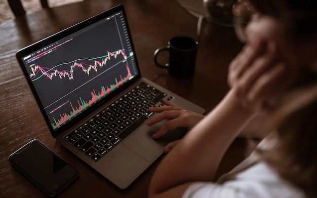 Jonge vrouw kijkt naar de markt op haar laptop.