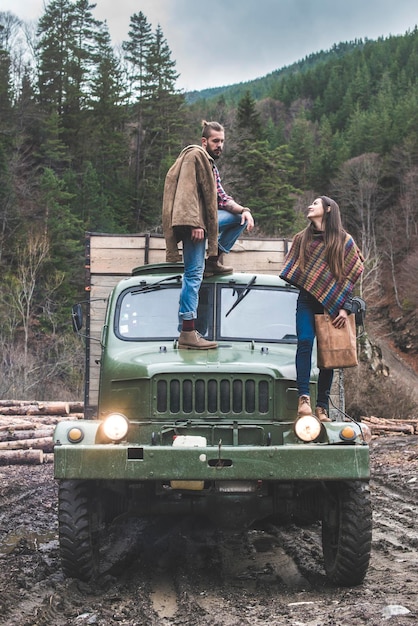 Foto jonge vrouw kijkt naar een man die op een vrachtwagen in het bos staat.