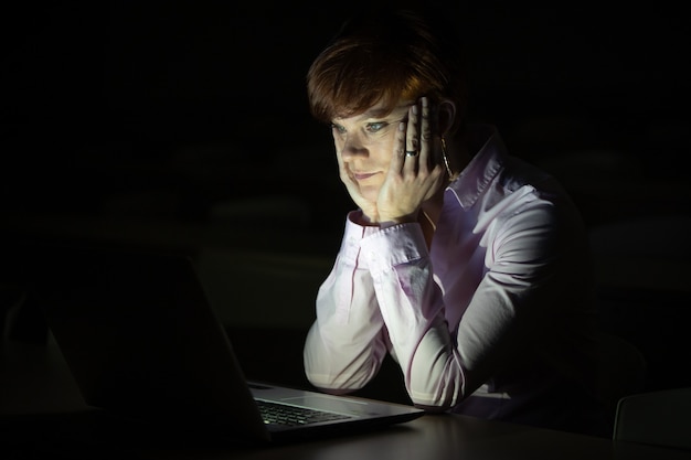jonge vrouw kijkt naar laptop in een donkere kamer