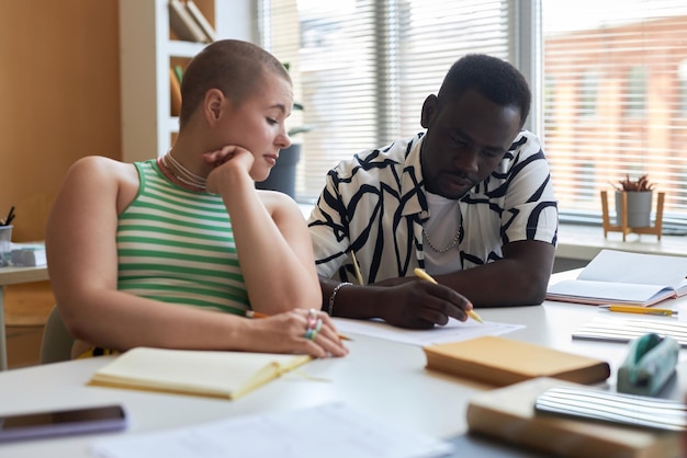 Jonge vrouw kijkt naar papier met aantekeningen van haar klasgenoot die ze haar uitlegt terwijl ze allebei aan een bureau zitten tijdens een les informatica