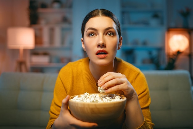 Jonge vrouw kijkt naar tv-films met popcorn Meisje brengt tijd thuis door