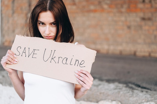 Jonge vrouw kijkt van onder haar voorhoofd naar de camera terwijl ze een poster vasthoudt over het beëindigen van de oorlog in Oekraïne