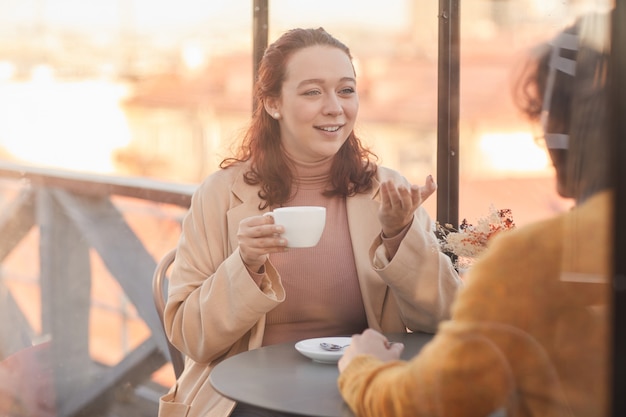 Jonge vrouw koffie drinken en praten met haar vriend tijdens hun bijeenkomst in café