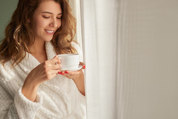 Jonge vrouw koffie drinken in de buurt van venster