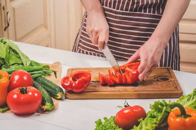 Jonge vrouw koken in de keuken thuis. Gezond eten. Eetpatroon. Dieet concept. Gezonde levensstijl. Thuis koken. Eten koken. Een vrouw snijdt een peper en groenten met een mes.