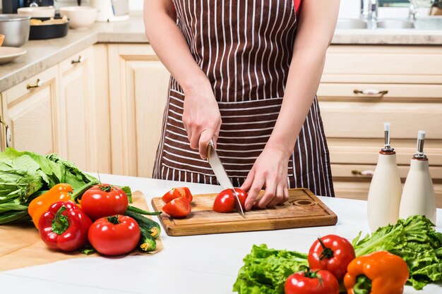Jonge vrouw koken in de keuken thuis. Gezond eten. Eetpatroon. Dieet concept. Gezonde levensstijl. Thuis koken. Eten koken. Een vrouw snijdt een tomaat en groenten met een mes.