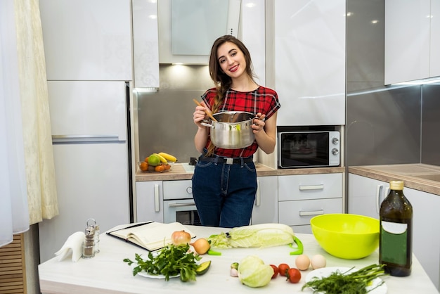 Jonge vrouw koken voedsel in een pot in de keuken.