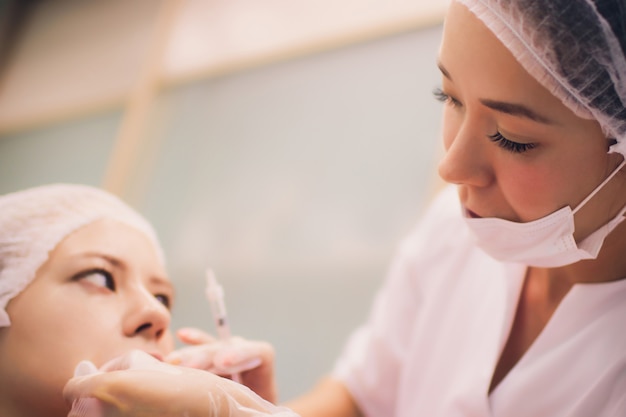 Jonge vrouw krijgt een injectie in haar lippen in schoonheidssalon. Schoonheid injecties - vrouw liggend in het kantoor van de schoonheidsspecialiste. Lippen verhogen door hyaluronzuur, contourprocedure, revitalisatie