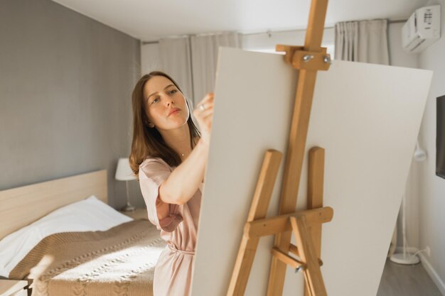 Jonge vrouw kunstenaar schilderen op canvas op de ezel thuis in slaapkamer kunst en creativiteit concept