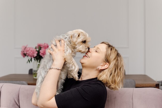 Jonge vrouw kust Yorkshire Terriër hond, in haar woonkamer op roze sofa. Ze zijn gelukkig samen.