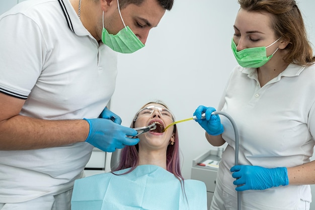 Jonge vrouw laat haar tanden behandelen door een mannelijke tandarts en een vrouwelijke assistent tijdens een afspraak bij een tandheelkundige kliniek