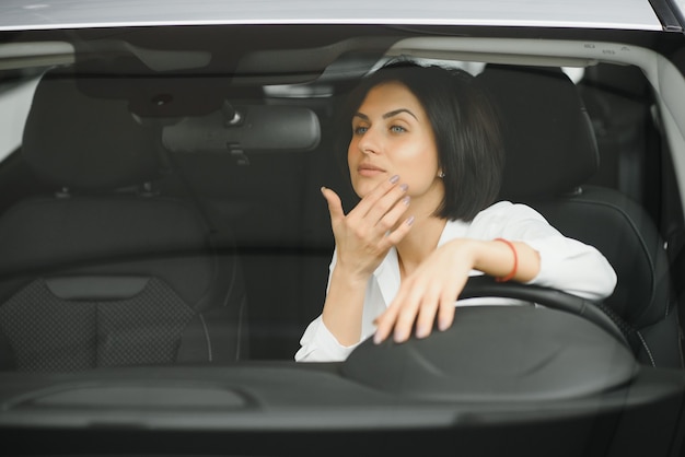 Jonge vrouw lachend in haar nieuwe auto in een showroom