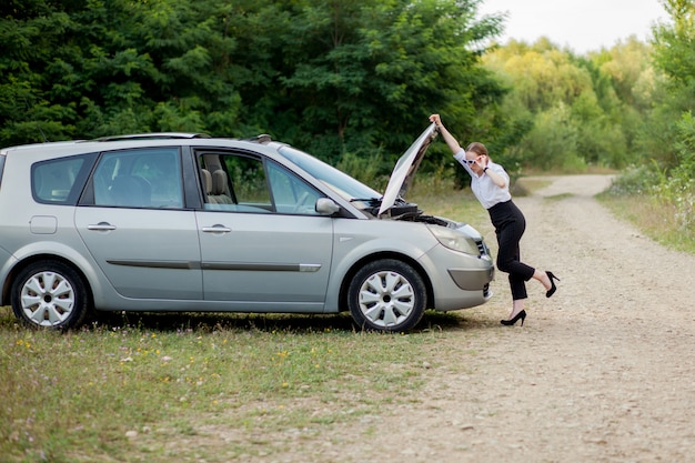 Jonge vrouw langs de weg nadat haar auto kapot is gegaan. ze deed de motorkap open om de schade te zien