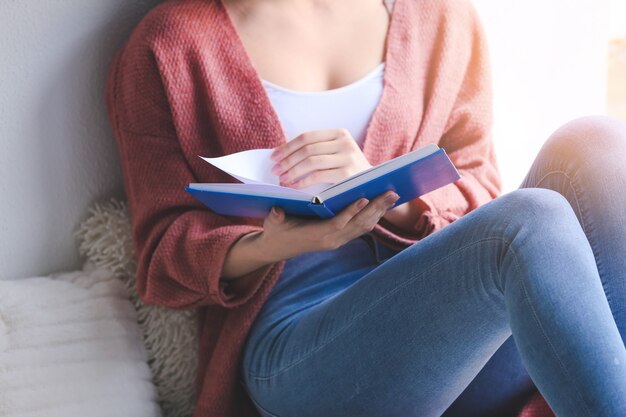 Jonge vrouw leesboek thuis, close-up