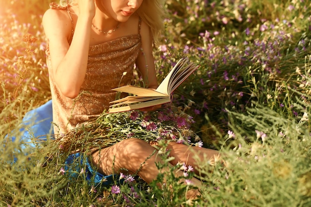 Jonge vrouw leest een boek in het veld in de natuur. zomer avond. Abstracte achtergrond.