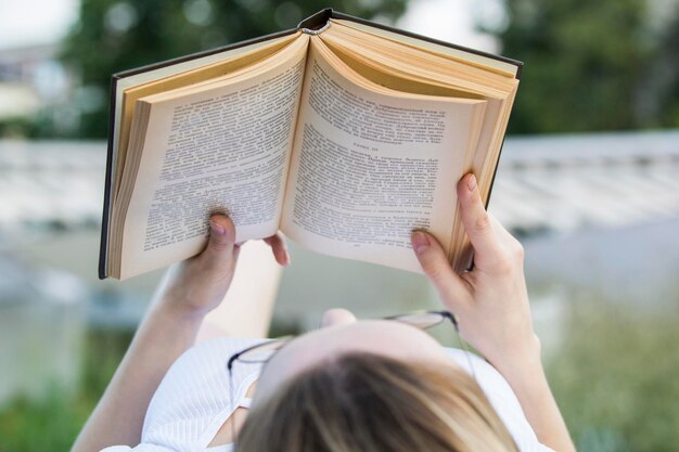 Jonge vrouw leest een oud boek dat op zomerdag buiten ligt, close-up