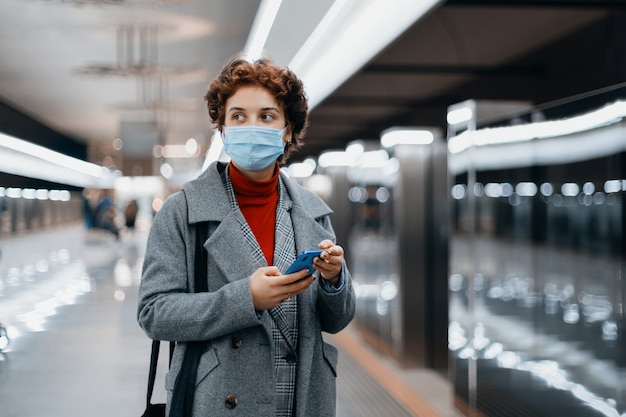 Jonge vrouw leest een sms-bericht op een metroperron