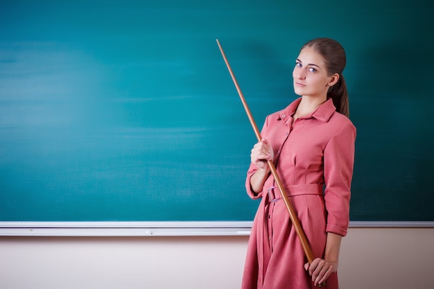 Jonge vrouw leraar staat op een schoolbord met een wijzer. Leraren dag.