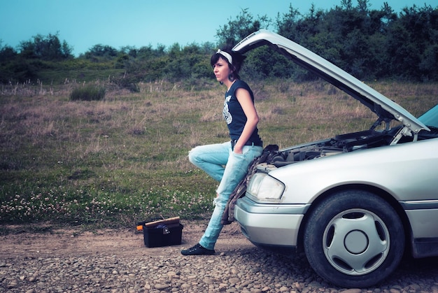 Foto jonge vrouw leunt op een beschadigde auto op het platteland