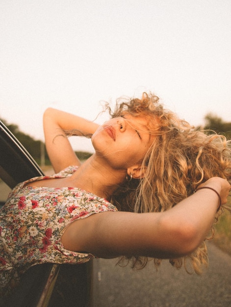 Jonge vrouw leunt van het raam van de auto tegen de heldere lucht