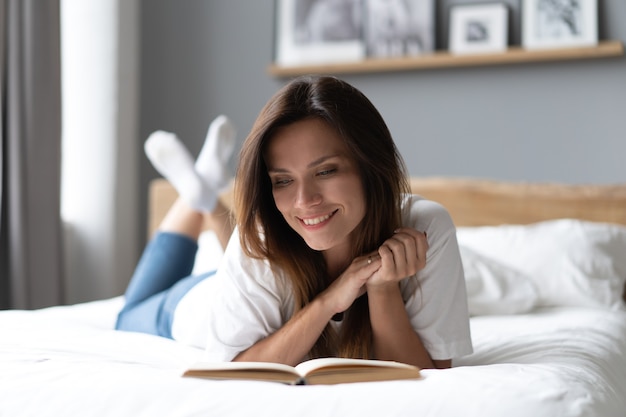 Jonge vrouw liggend op bed en boek thuis lezen.