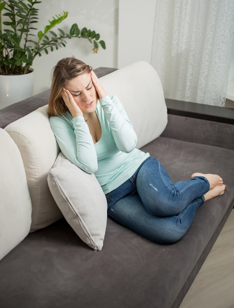 Jonge vrouw liggend op de bank en lijdend aan hoofdpijn