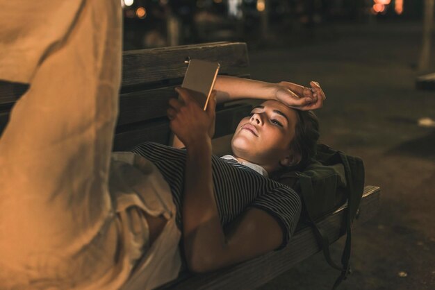 Jonge vrouw liggend op de bank 's nachts met behulp van mobiele telefoon