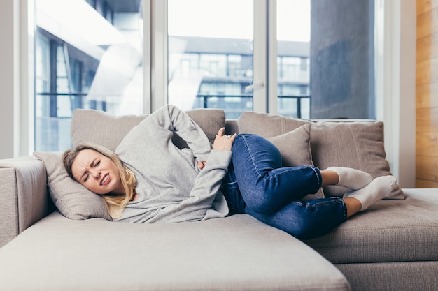 Jonge vrouw liggend op de bank thuis met ernstige buikpijn