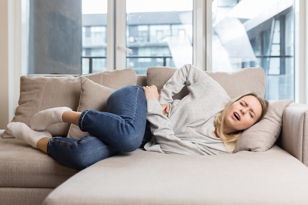 Jonge vrouw liggend op de bank thuis met ernstige buikpijn