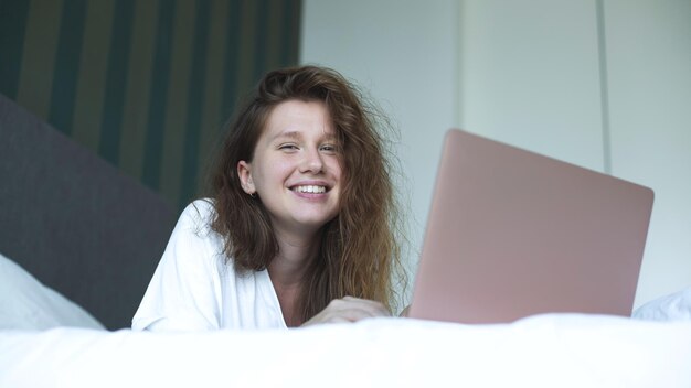 Jonge vrouw ligt en gebruikt laptop in bed in de ochtend concept online leren werk winkelen