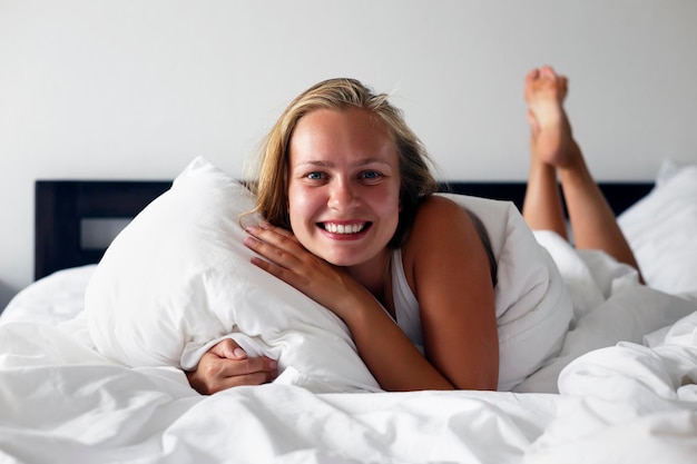 Jonge vrouw ligt in bed met een witte onderbroek na het wakker worden en glimlacht naar de kijker