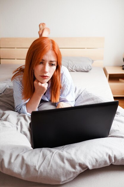 Jonge vrouw ligt op bed met een laptop.