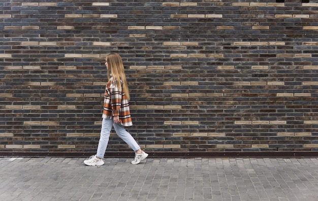 Foto jonge vrouw loopt de straat af tegen een bakstenen muur