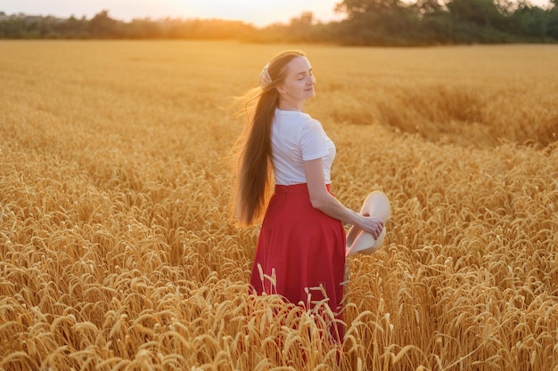 Jonge vrouw loopt door het veld van rijpe tarwe bij zonsondergang Natuurlijke schoonheid