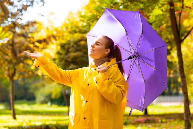 Jonge vrouw loopt op een zonnige dag gouden herfst in het park meisje met paraplu en regenjas genieten van...