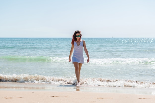 Jonge vrouw loopt op het strand in een witte jurk