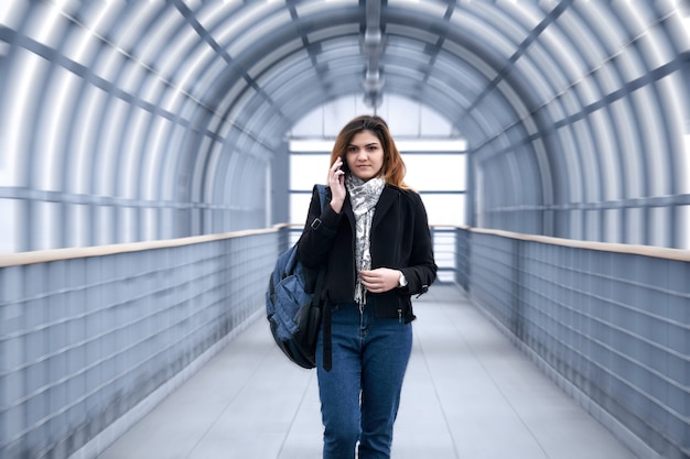 Jonge vrouw loopt snel langs een overdekt voetgangersviaduct, telefoneert en glimlacht