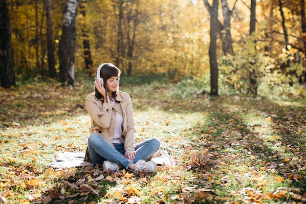 Jonge vrouw luisteren naar muziek met een koptelefoon in de herfst bos