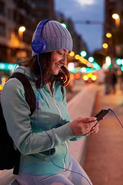 Jonge vrouw luistert naar muziek op een koptelefoon met stadslichten in de schemering