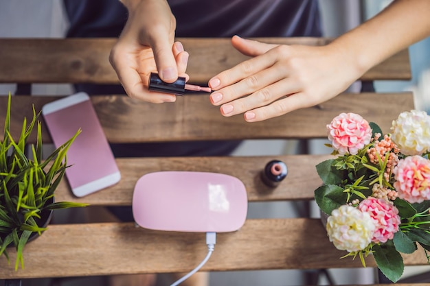 Jonge vrouw maakt manicure met gellak en UV-lamp in roze tinten