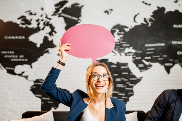 Foto jonge vrouw manager droomt met kleurrijke bubbel boven het hoofd zittend op kantoor met wereldkaart op de achtergrond