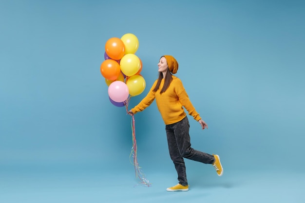 Jonge vrouw meisje in trui hoed poseren geïsoleerd op blauwe achtergrond in studio. Vakantie verjaardagsfeestje, mensen emoties concept. Bespotten kopie ruimte. Vieren houd kleurrijke luchtballonnen opzij kijkend.