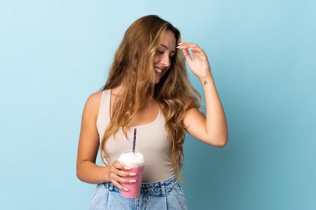 Jonge vrouw met aardbeimilkshake die bij het blauwe muur lachen wordt geïsoleerd