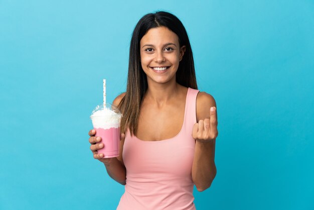 Jonge vrouw met aardbeimilkshake die geldgebaar maakt