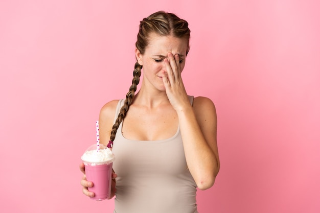 Jonge vrouw met aardbeimilkshake die op roze muur met vermoeide en zieke uitdrukking wordt geïsoleerd