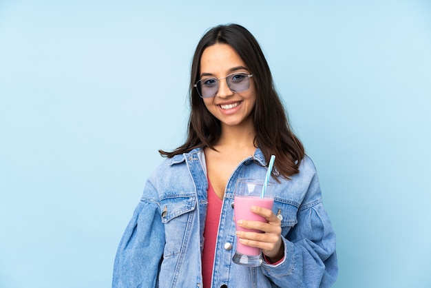 Jonge vrouw met aardbeimilkshake op geïsoleerd blauw die de wapens in frontale positie gekruist houden