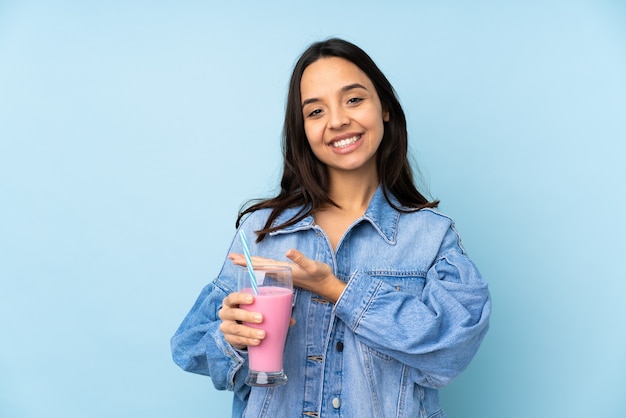 Jonge vrouw met aardbeimilkshake over geïsoleerde blauwe muur die een idee voorstelt terwijl het glimlachen naar kijkt